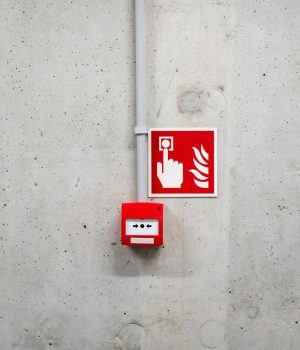 Red emergency fire alarm on a gray concrete wall in Poznań, enhancing safety awareness.